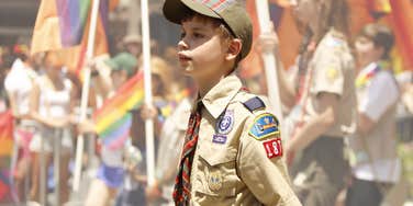 Boy scout holding LGBTQ+ flag while walking in a parade. 